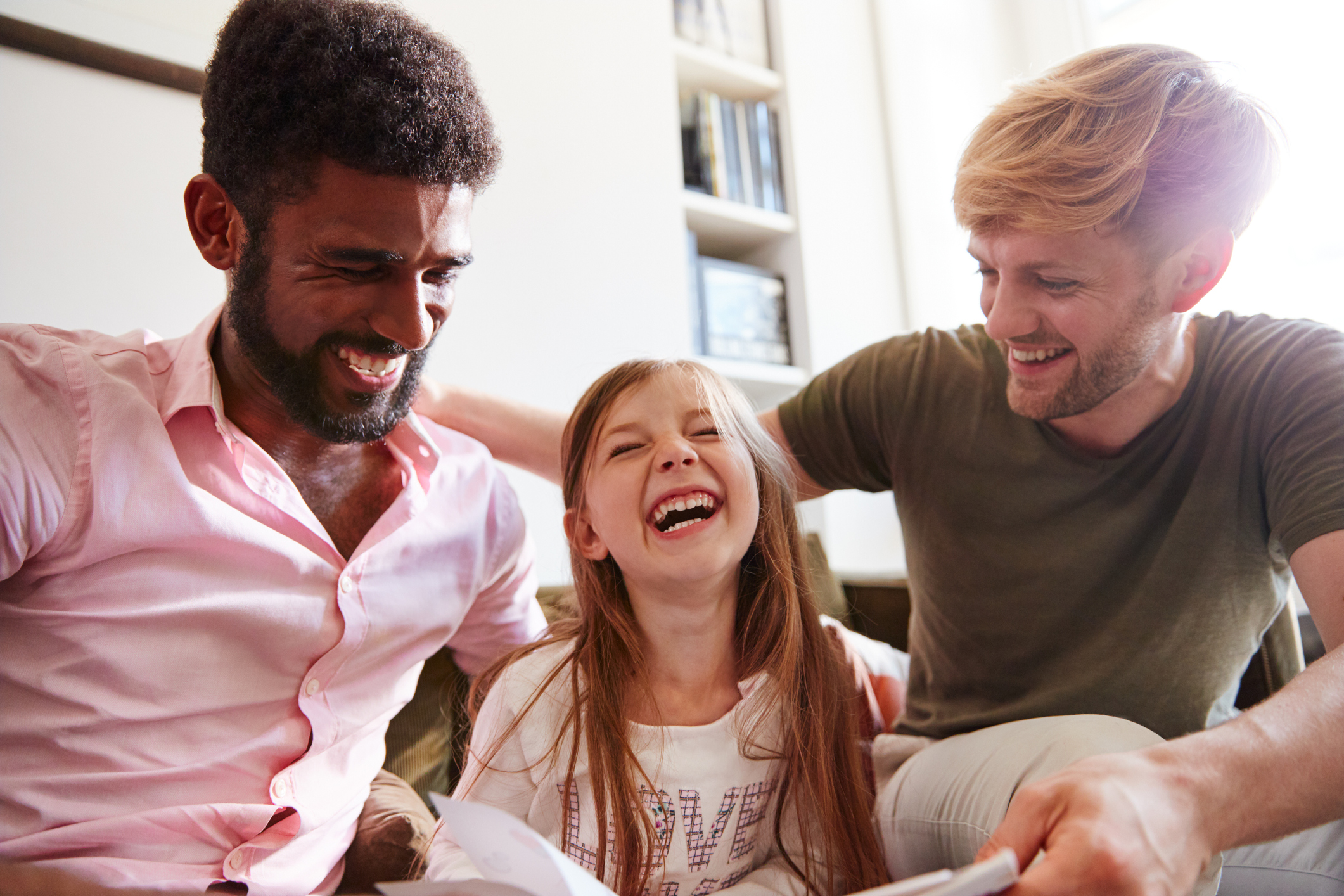 Two dads read a book with daughter